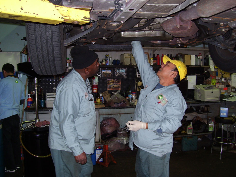 Mechanic3 2 Mechanics looking under a car that is on a car lift in a shop